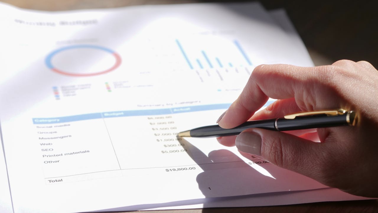 Mano che tiene una penna, analizzando il budget con grafici e fogli con diagrammi.
